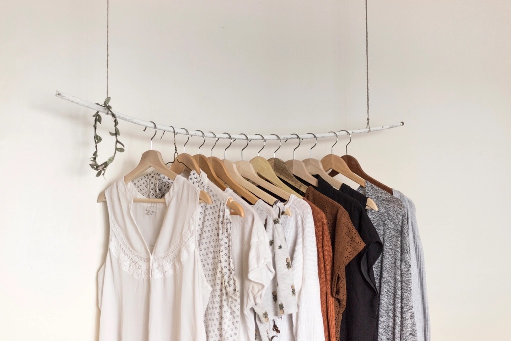 Neutral-coloured clothes hanging on a simple rail against a white wall